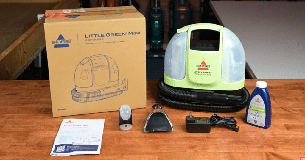 Bissell Little Green Mini Cordless spot cleaner with attachments at Vacuum Wars | Vacuum Wars Bissell Little Green Mini Cordless spot cleaner with its box, Tough Stain Tool, HydroRinse hose-cleaning tool, charger, cleaning formula, and documentation.