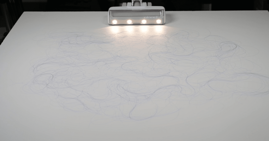 Bissell Powerclean Cordless Vacuum 4173 Hair Test at Vacuum Wars 1 | Vacuum Wars A cordless vacuum with floorhead lights approaching hair on a hard floor.