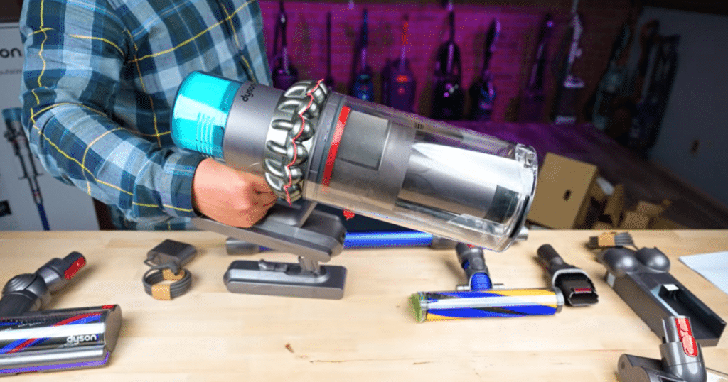 Handheld Cordless Vacuum Head | Vacuum Wars Person holding a bulky cordless stick vacuum motor unit above a table of floorheads and cleaning attachments.