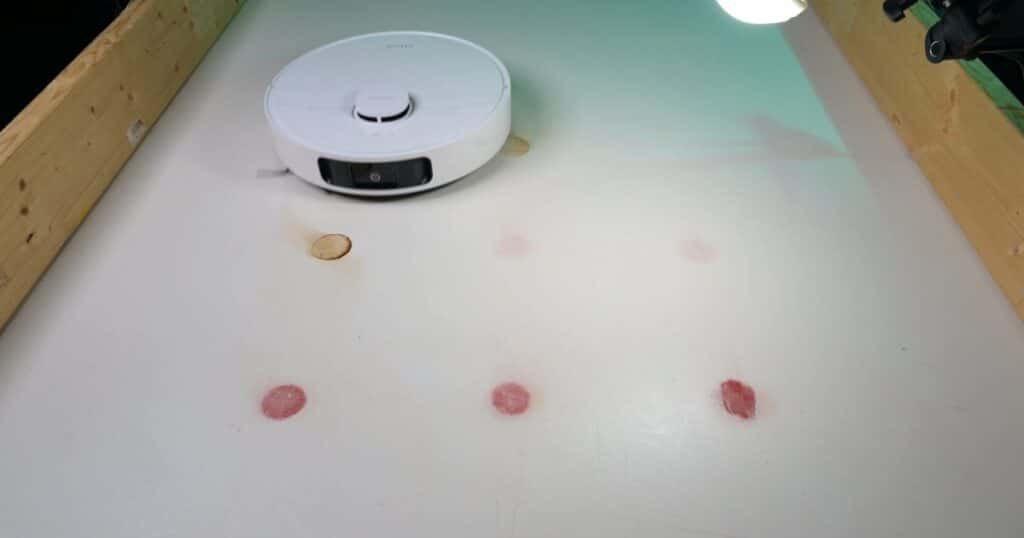 | Vacuum Wars Dreame D30 Ultra robot vacuum undergoing a dried-stain test on a hard floor with several red and brown stains visible.