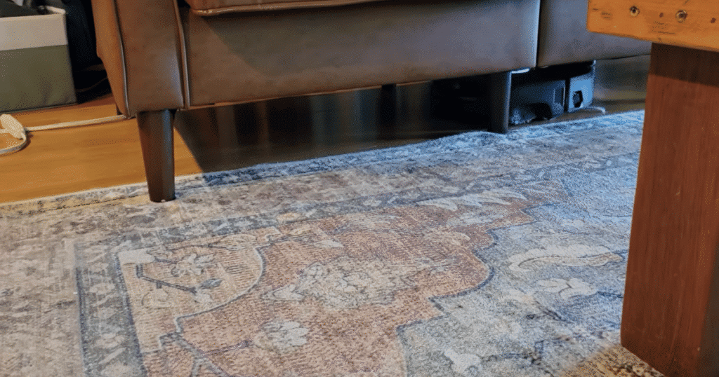 Narwal Flow 2 Home clearance | Vacuum Wars Narwal Flow 2 robot vacuum cleaning underneath a low-clearance sofa beside an area rug during long-term home testing.
