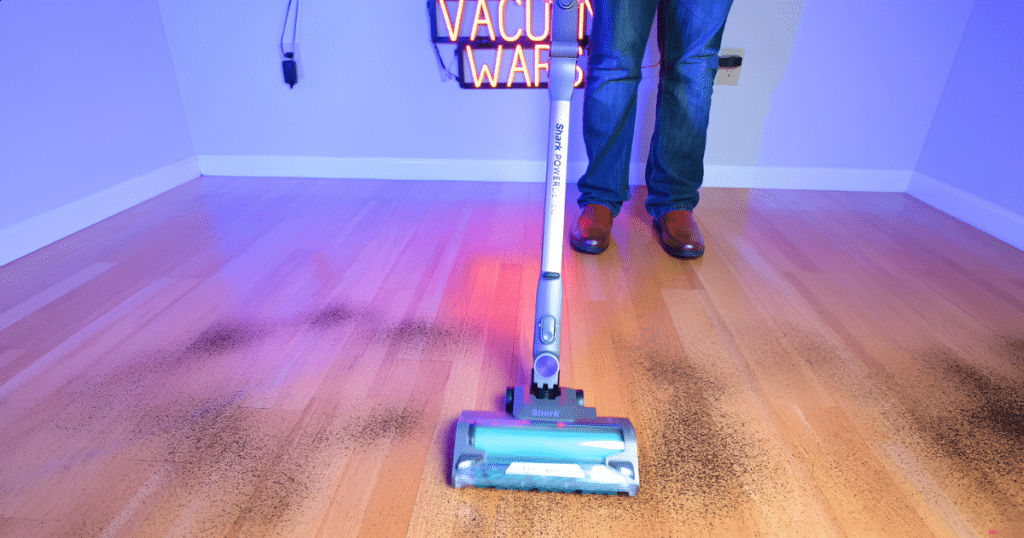 _Shark Cordless Powerdetect Clean and Empty Vacuum on Hard Floor at Vacuum Wars | Vacuum Wars Shark PowerDetect Clean and Empty cordless vacuum picking up fine debris from a hard floor with its DuoClean floorhead and LED lights illuminated.