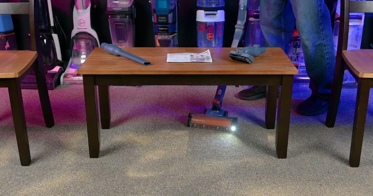 | Vacuum Wars Shark PowerDetect Speed Clean & Empty using its floorhead light to illuminate debris while cleaning beneath a table.
