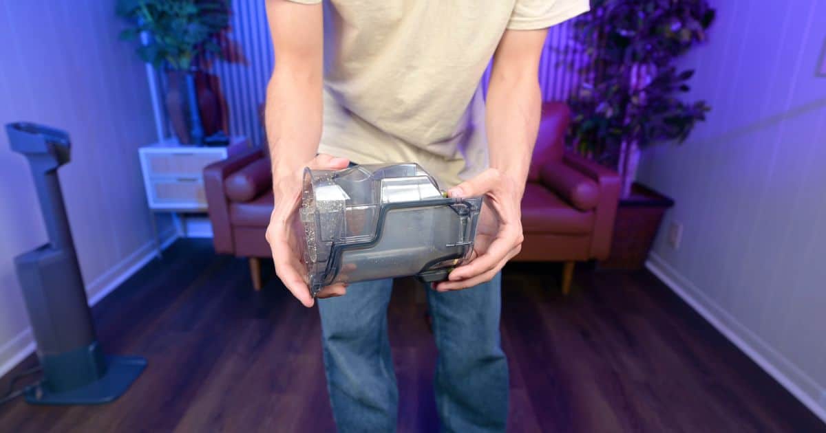 Shark-PowerDetect-Speed-Review-dustbin | Vacuum Wars Person holding a transparent vacuum cleaner dustbin in a living room setting with purple lighting