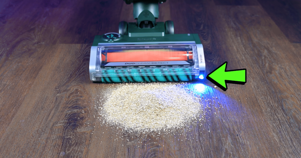 _Shark Transformer Reveal Light Vacuum Wars | Vacuum Wars A vacuum cleaner floor head with a bright blue LED light, cleaning a pile of beige dust on a wooden floor.