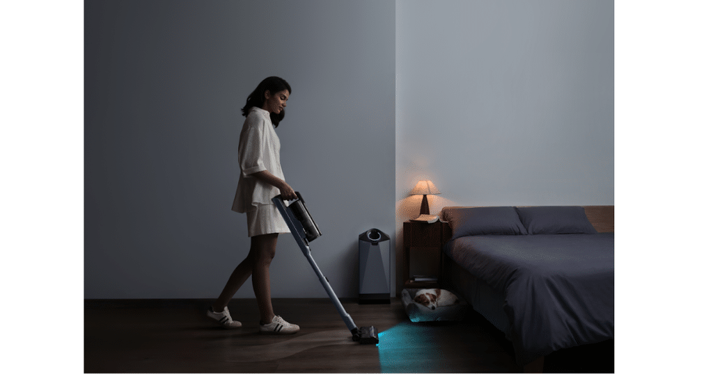 Narwal V50 Cube at Home | Vacuum Wars Person using a Narwal V50 Cube cordless stick vacuum to clean a bedroom floor beside a bed and compact docking station.