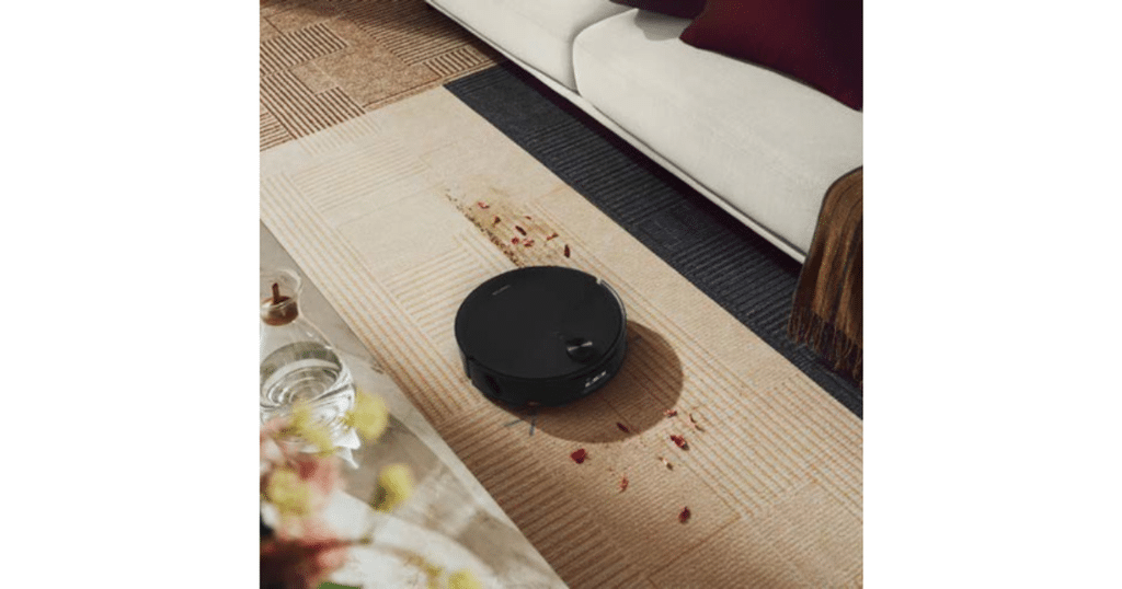 Roborock Saros 20 Flow Complete Qrevo Edge 3 Pro Vacuuming | Vacuum Wars Black Roborock Saros 20 Flow robot vacuum cleaning scattered debris from a patterned rug beside a sofa.