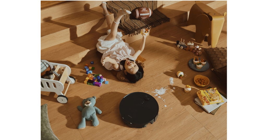 Roborock Saros 20 Flow Obstacle Avoidance at Home | Vacuum Wars Child lying on a wooden floor among scattered toys, with a black robotic vacuum cleaner nearby.