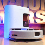 Yeedi C14 Pro+ in studio 150 | Vacuum Wars White robotic vacuum on its charging dock in a colorful neon-lit studio backdrop, suggesting a product photoshoot for smart cleaning devices.