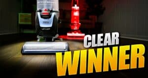 | Vacuum Wars Bissell Pet Hair Eraser Allergen Lift-Off 39883 upright vacuum in the foreground with the Bissell CleanView 2254 behind it and large “CLEAR WINNER” text.