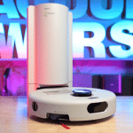 Dyson R1 Nurovi Dry in studio 150 | Vacuum Wars Small circular robot vacuum on a stage with pink and blue neon lights in the background.