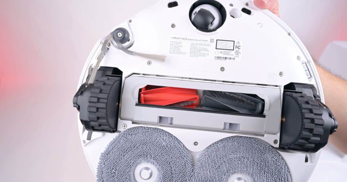 | Vacuum Wars Close-up of the underside of the Roborock Qrevo Edge 3 Pro, showing its red and black DuoDivide main brush, FlexiArm side brush, two gray circular mop pads, and large drive wheels.