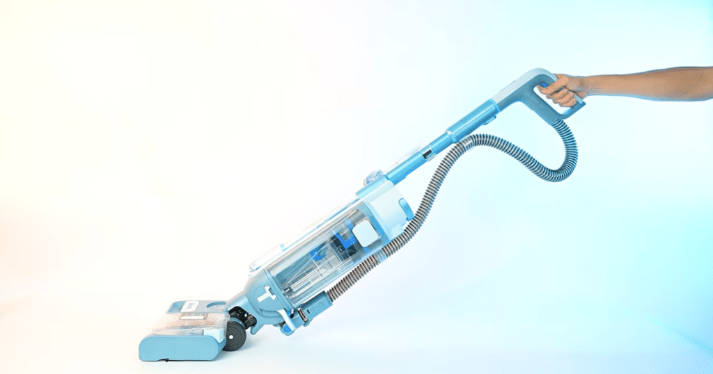 Shark AquaReach Wet Dry Vacuum in use art Vacuum Wars | Vacuum Wars Blue cordless vacuum cleaner being held by a hand, angled for cleaning, on a light gradient background.