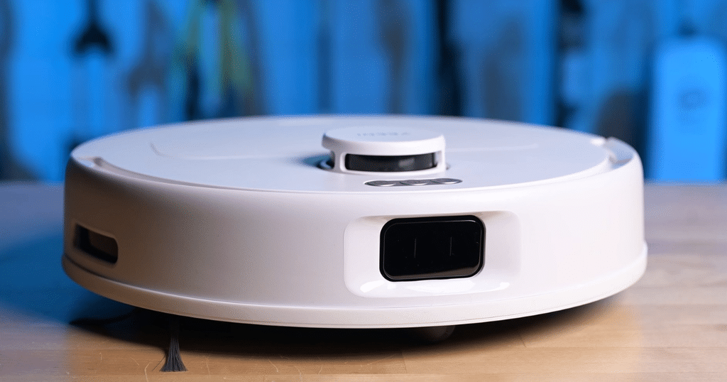 Yeedi C14 PRO Plus robot vacuum Vacuum Wars | Vacuum Wars White robotic vacuum on a wooden floor, close-up view showing its circular design and sensor window on the side.